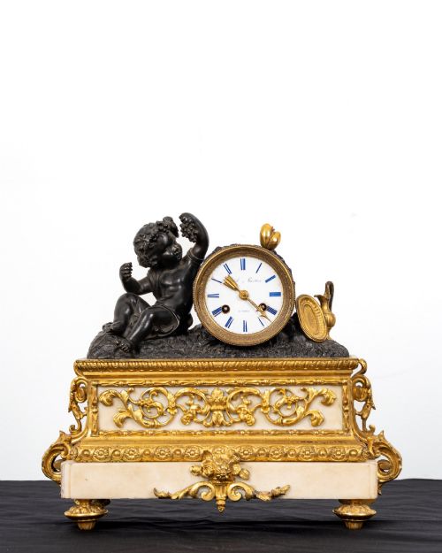 fig 1. A French 19th-century figural mantel clock with a patinated bronze cherub beside a circular white enamel dial on a gilt-bronze and marble base.