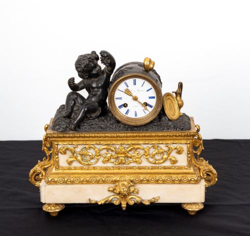 fig 2. A French 19th-century figural mantel clock with a patinated bronze cherub beside a circular white enamel dial on a gilt-bronze and marble base.