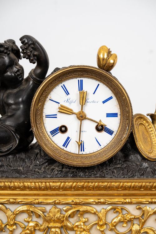 fig 5. A French 19th-century figural mantel clock with a patinated bronze cherub beside a circular white enamel dial on a gilt-bronze and marble base.