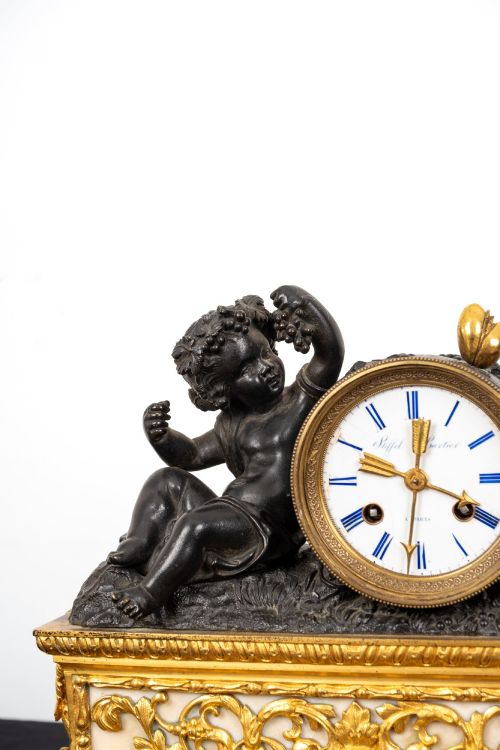 fig 6. A French 19th-century figural mantel clock with a patinated bronze cherub beside a circular white enamel dial on a gilt-bronze and marble base.