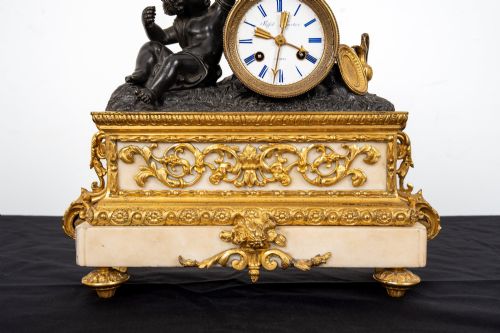 fig 7. A French 19th-century figural mantel clock with a patinated bronze cherub beside a circular white enamel dial on a gilt-bronze and marble base.