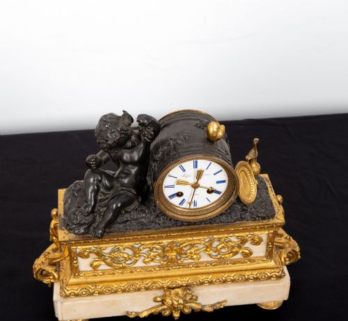 fig 8. A French 19th-century figural mantel clock with a patinated bronze cherub beside a circular white enamel dial on a gilt-bronze and marble base.