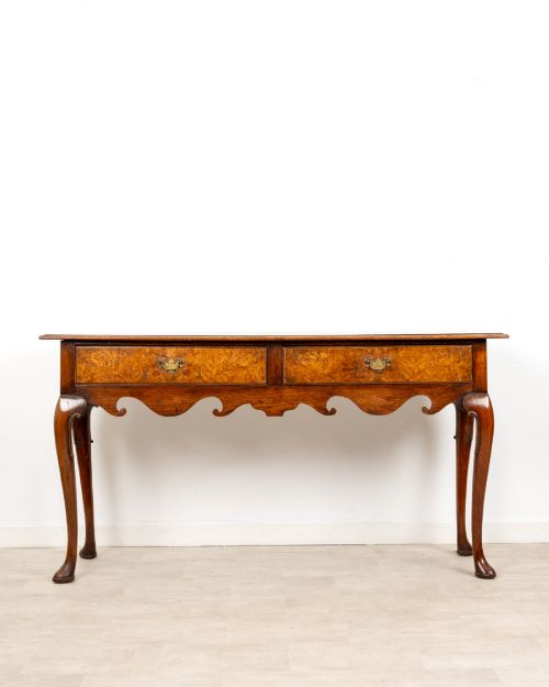 fig 1. A Queen Anne style burr walnut console table featuring two drawers, a shaped apron, and four slender cabriole legs terminating in pad feet.