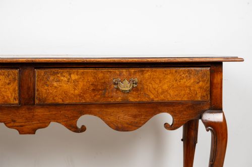 fig 3. A Queen Anne style burr walnut console table featuring two drawers, a shaped apron, and four slender cabriole legs terminating in pad feet.