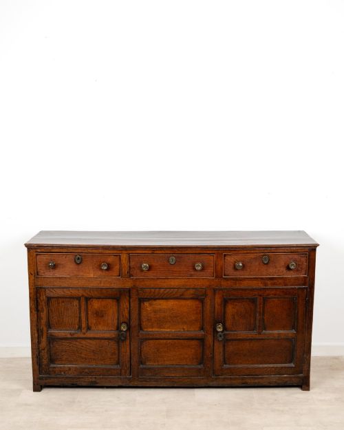 fig 2. A Georgian antique oak dresser base featuring three upper drawers with metal keyhole escutcheons above three panelled cupboard doors.