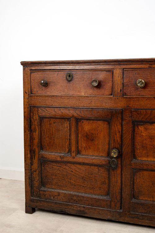fig 6. A Georgian antique oak dresser base featuring three upper drawers with metal keyhole escutcheons above three panelled cupboard doors.
