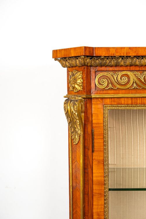 fig 5. A large veneered display cabinet featuring gilt-bronze mounts, glazed twin doors, glass shelving, and a fabric-lined interior.