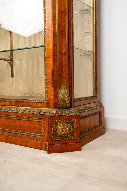 fig 6. A large veneered display cabinet featuring gilt-bronze mounts, glazed twin doors, glass shelving, and a fabric-lined interior.