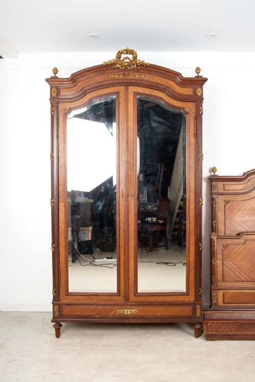fig 2. A French Louis XVI Revival mahogany bedroom suite comprising a mirrored two-door armoire, a matching bedframe with parquetry detailing, and a marble-topped bedside table with gilded bronze mounts.