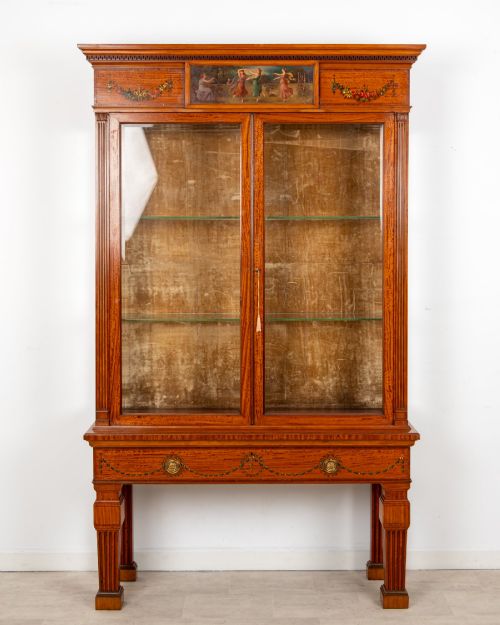 fig 1. An antique Edwardian painted satinwood display cabinet featuring two glazed doors, glass shelves, fluted tapering legs, and classical hand-painted figurative and floral panels.