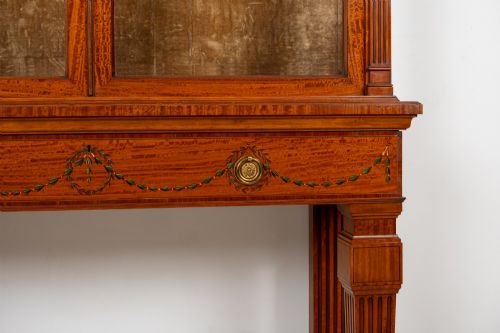 fig 3. An antique Edwardian painted satinwood display cabinet featuring two glazed doors, glass shelves, fluted tapering legs, and classical hand-painted figurative and floral panels.