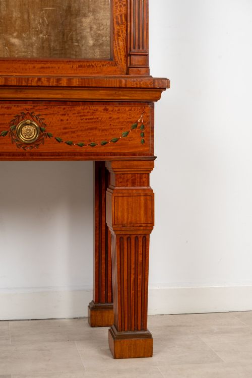 fig 4. An antique Edwardian painted satinwood display cabinet featuring two glazed doors, glass shelves, fluted tapering legs, and classical hand-painted figurative and floral panels.