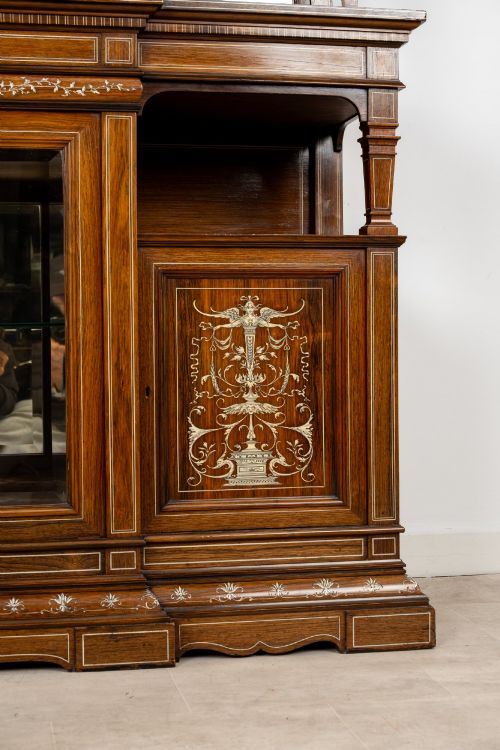 fig 4. A large late Victorian rosewood display cabinet featuring intricate inlay work, glazed upper and lower doors, an arched pediment, and mirrored back panels.
