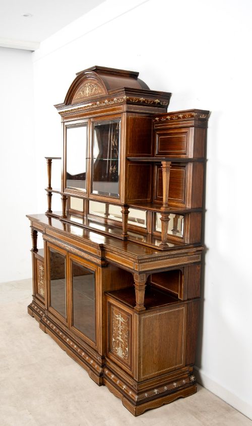 fig 7. A large late Victorian rosewood display cabinet featuring intricate inlay work, glazed upper and lower doors, an arched pediment, and mirrored back panels.