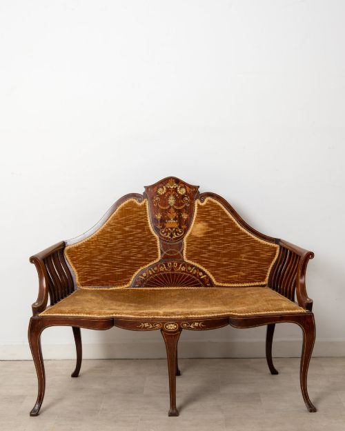 fig 1. An Edwardian mahogany settee featuring floral marquetry inlay on a central back panel, slatted arms, cabriole legs, and gold-brown velvet upholstery.
