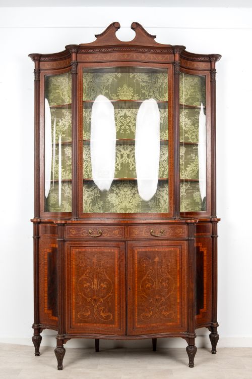 fig 1. An Edwardian mahogany display cabinet featuring satinwood marquetry inlay, glazed upper doors with green fabric lining, and turned legs.