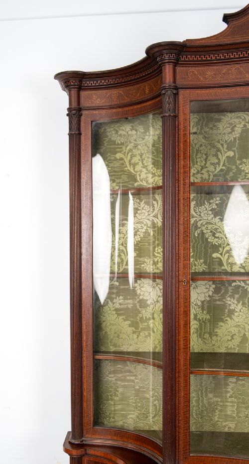 fig 4. An Edwardian mahogany display cabinet featuring satinwood marquetry inlay, glazed upper doors with green fabric lining, and turned legs.