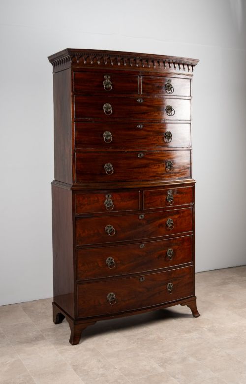 fig 1. A tall Victorian bow front mahogany chest on chest featuring multiple drawer tiers with brass ring handles and upper cornice trim.