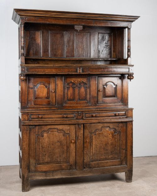 fig 1. A dark oak three-tier Welsh cwpwrdd tridarn featuring an open upper canopy, middle cupboard section with raised arch panels and turned pillars, and a base cupboard with two drawers.