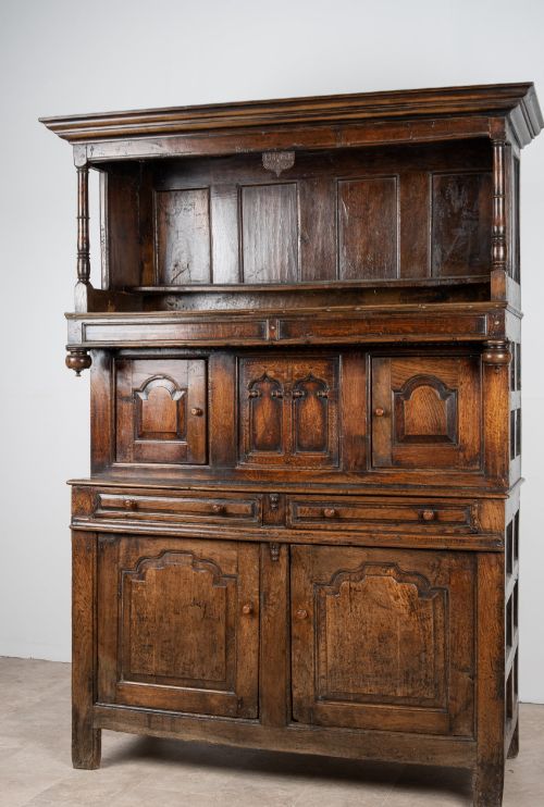 fig 3. A dark oak three-tier Welsh cwpwrdd tridarn featuring an open upper canopy, middle cupboard section with raised arch panels and turned pillars, and a base cupboard with two drawers.