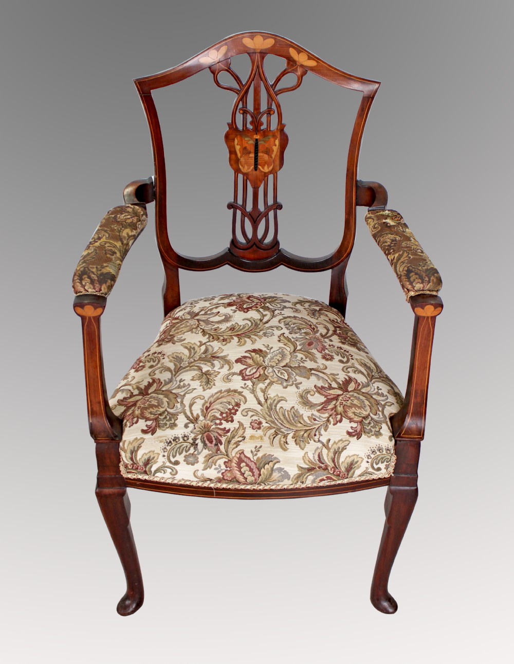An antique mahogany Art Nouveau open armchair featuring stylized floral marquetry inlay on the backrest and a woven floral fabric upholstered seat.