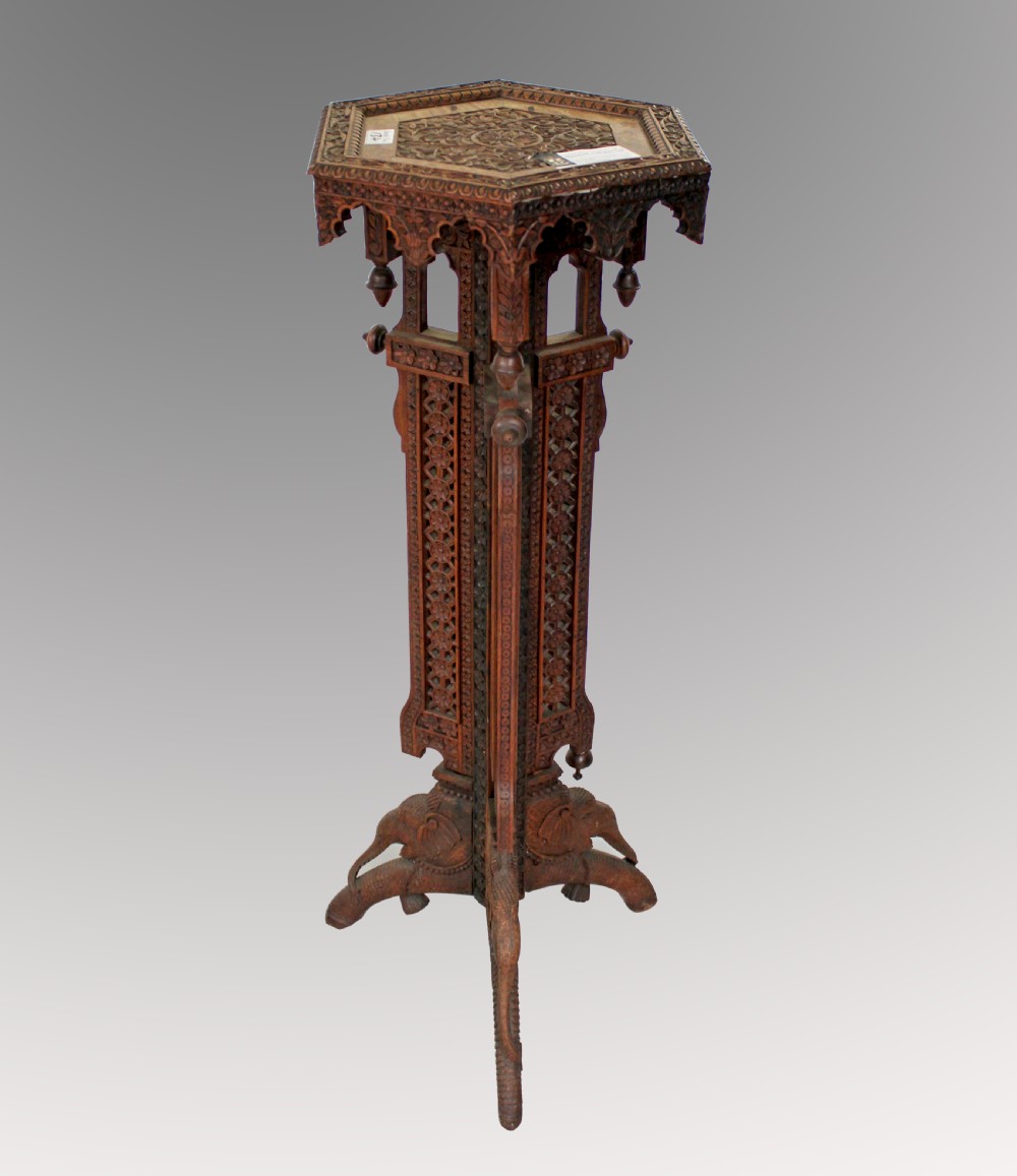 A tall dark brown wooden plant stand featuring intricate pierced fretwork carving, turned finials, and legs shaped like elephant heads.