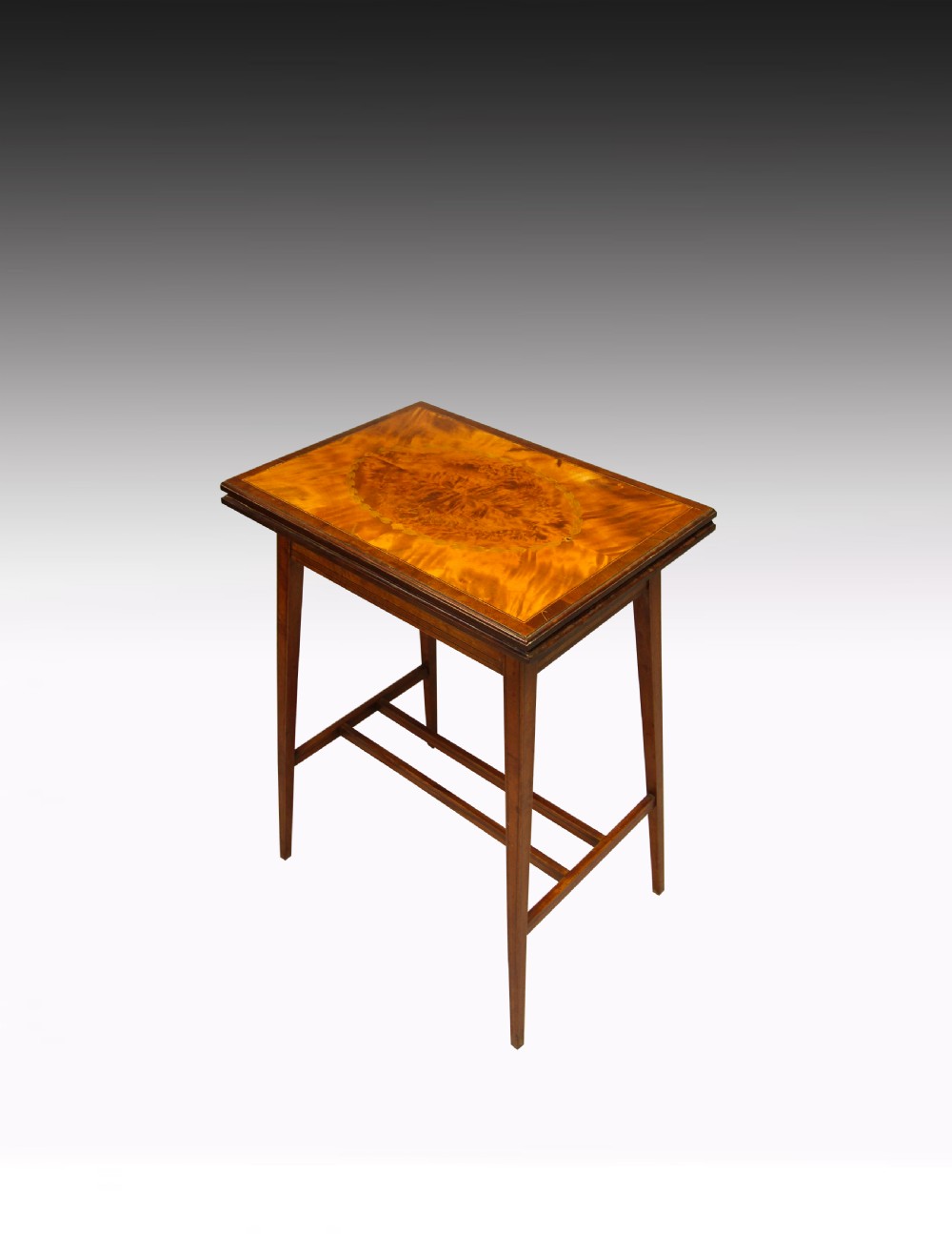 A rectangular antique satinwood card table featuring a central oval marquetry motif, crossbanded border, and tapered legs supported by an H-stretcher.