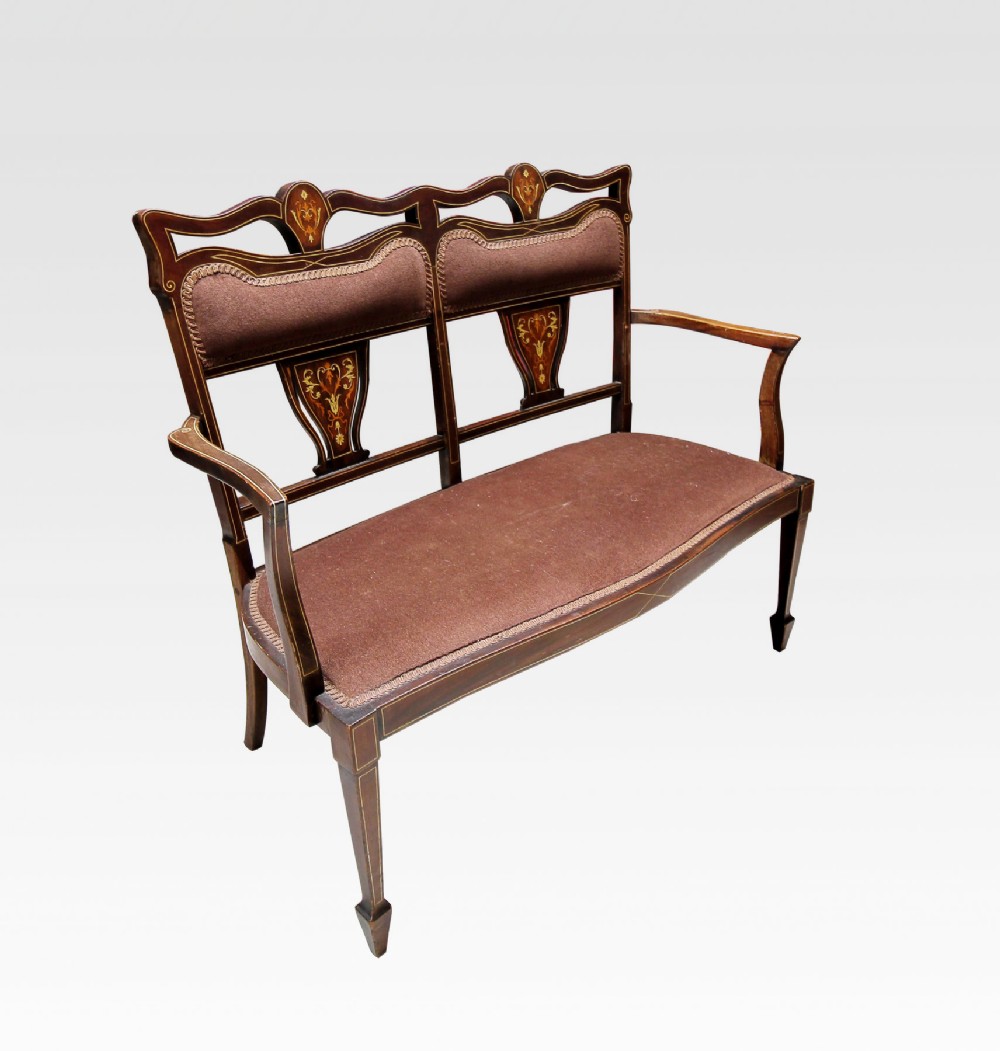 A late Victorian mahogany settee with floral marquetry inlay, slender shaped arms, tapered legs, and brown fabric upholstered seat and back pads.