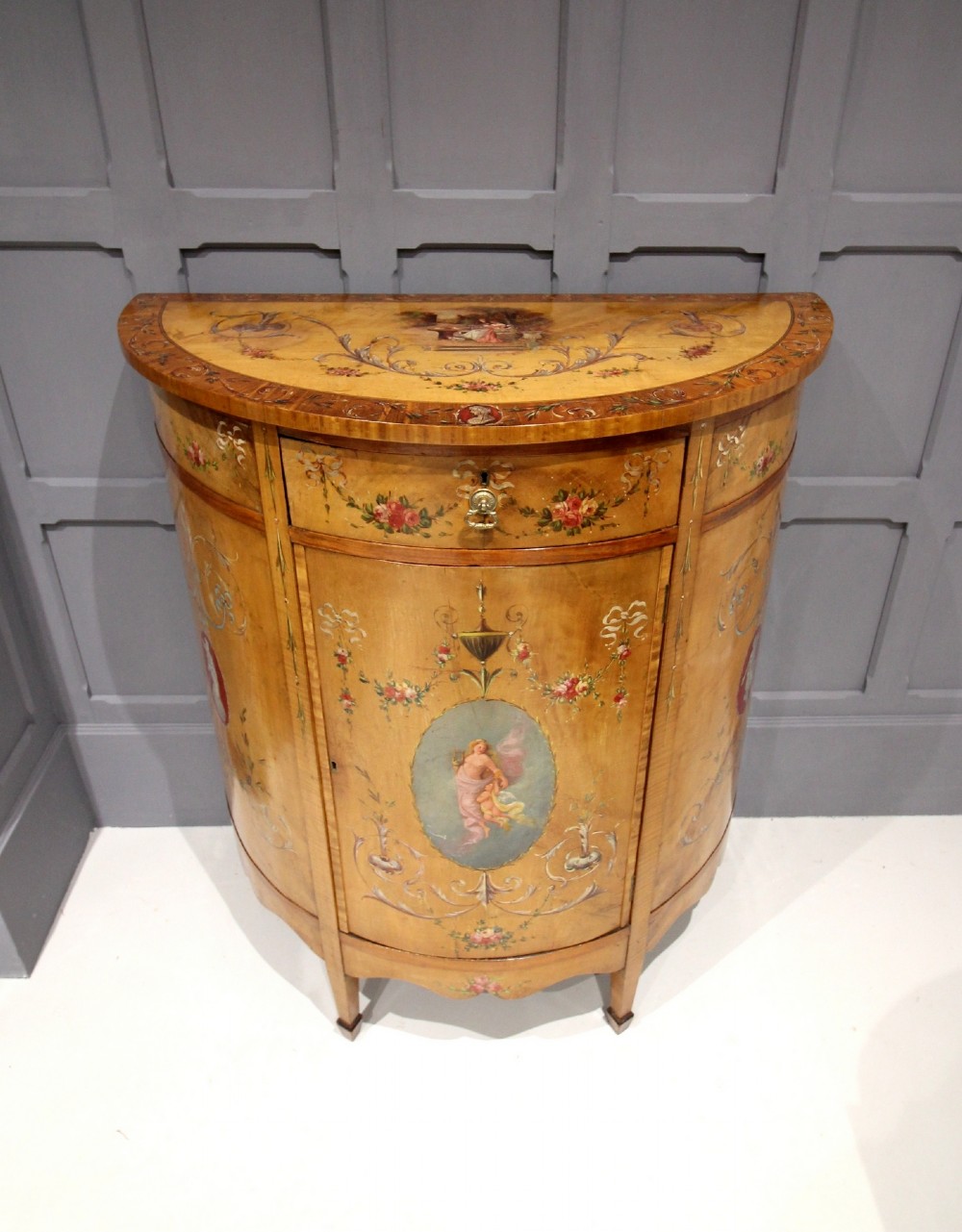 A SATINWOOD PAINTED DEMI LUNE SIDE CABINET 