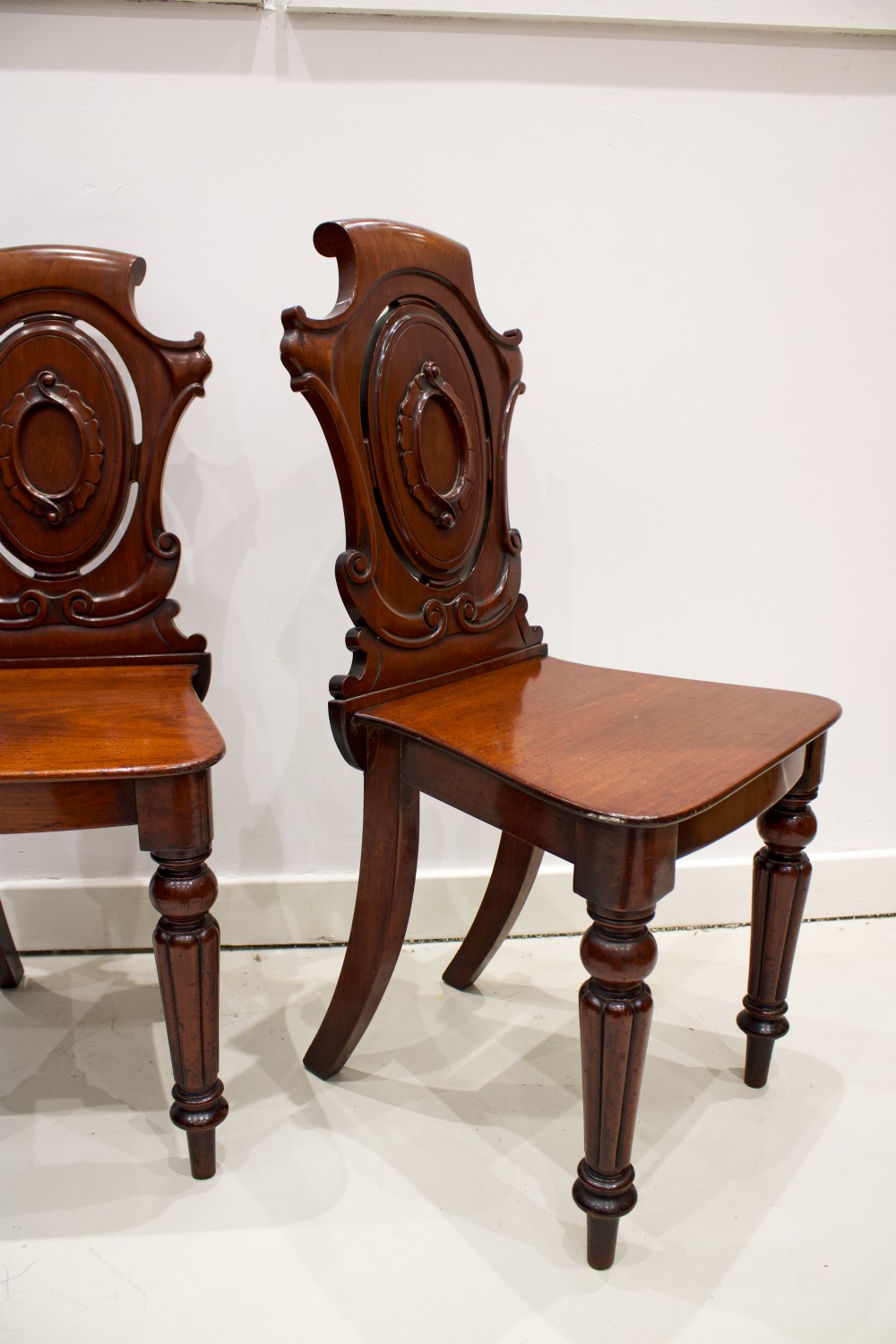A pair of 19th-century mahogany hall chairs with carved oval cartouche backs, flat timber seats, and turned front legs. View III