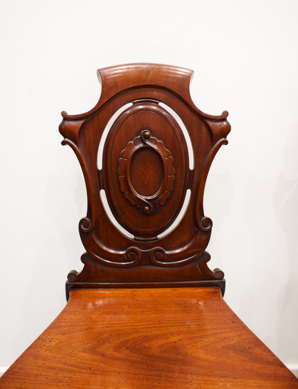 A pair of 19th-century mahogany hall chairs with carved oval cartouche backs, flat timber seats, and turned front legs. View IV