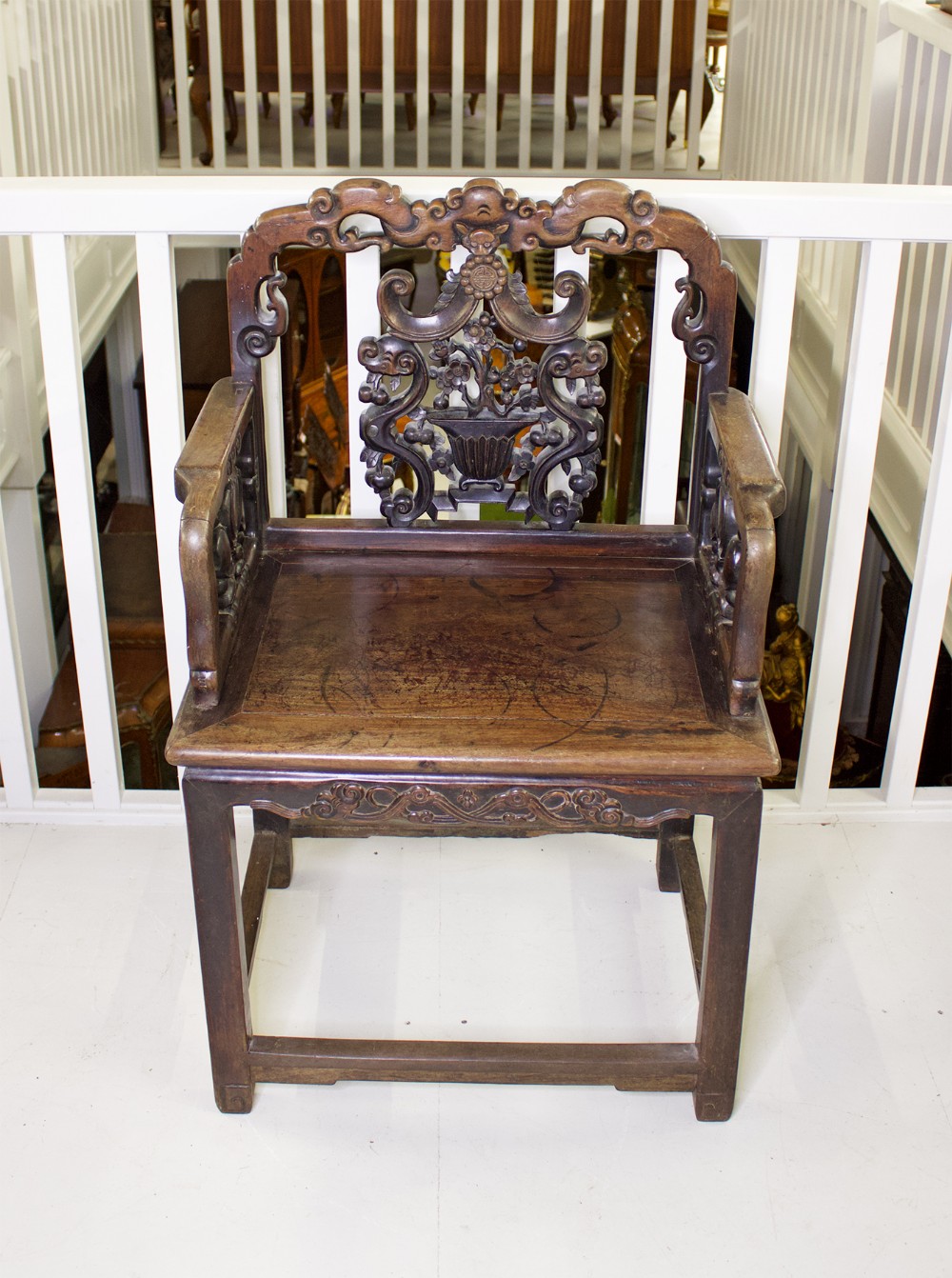 A 19th-century Chinese dark hardwood armchair featuring an intricately carved openwork splat back, shaped armrests, and square legs.