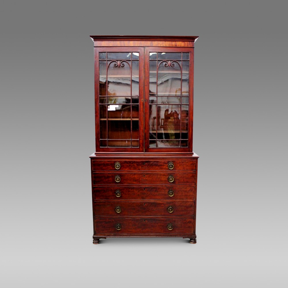 A William IV Cuban mahogany secretaire bookcase featuring a two-door glazed upper section with decorative glazing bars above a chest of drawers with brass handles.