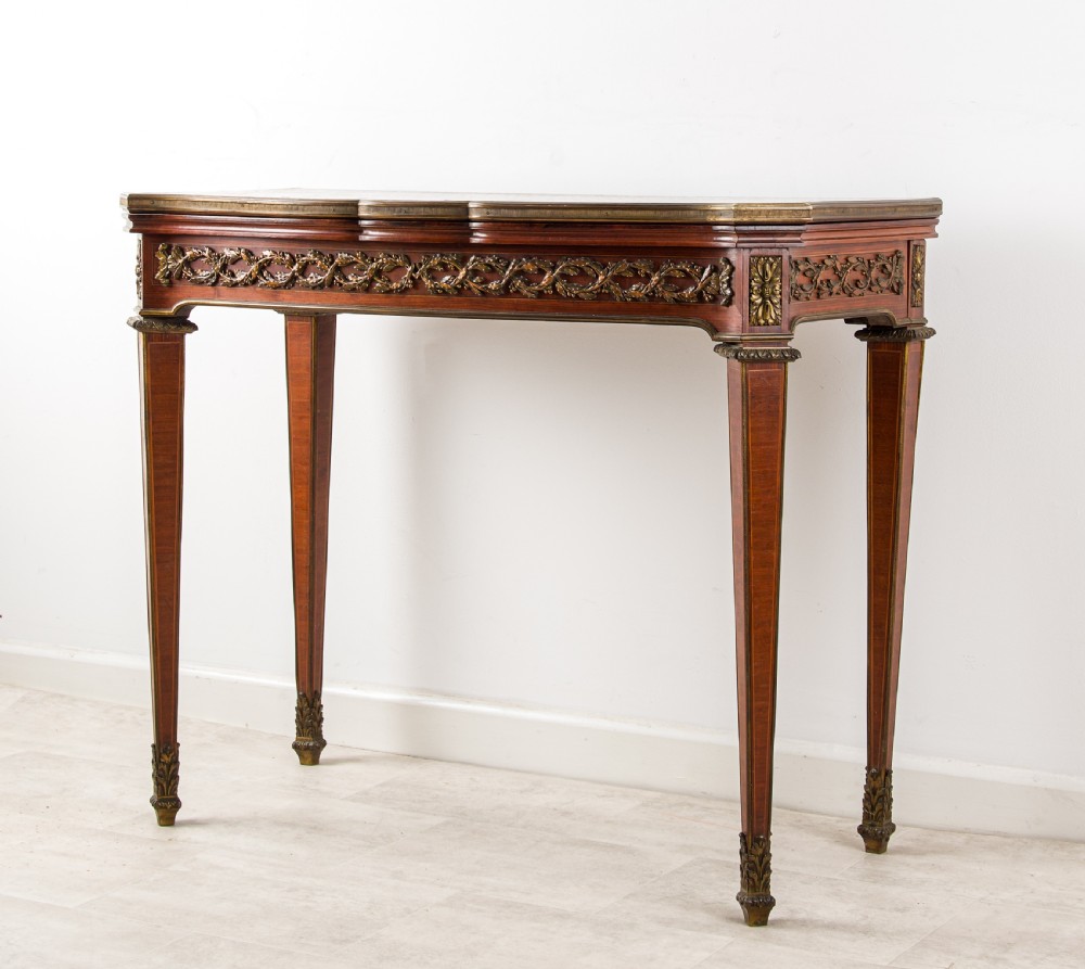 A French Louis XVI style games table featuring a parquetry fold-over top, foliage ormolu frieze, and square tapered legs with gilt mounts. View II
