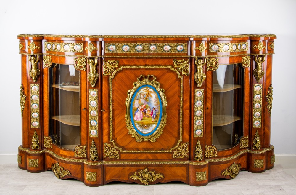 An antique kingwood breakfront credenza decorated with ornate gold ormolu mounts, central painted porcelain plaques, and two glazed side cabinet doors.