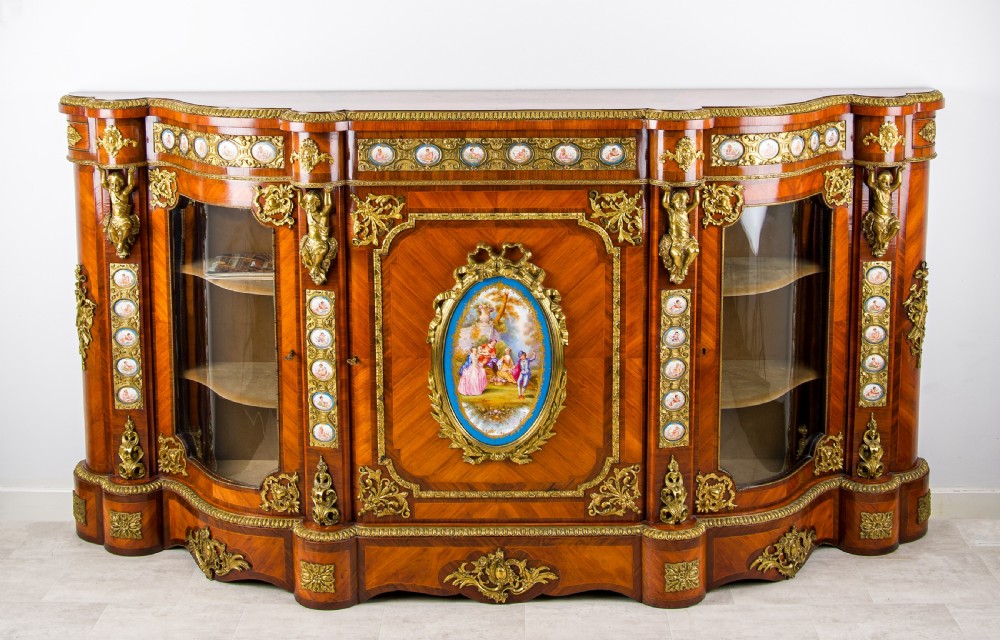 An antique kingwood breakfront credenza decorated with ornate gold ormolu mounts, central painted porcelain plaques, and two glazed side cabinet doors. View II
