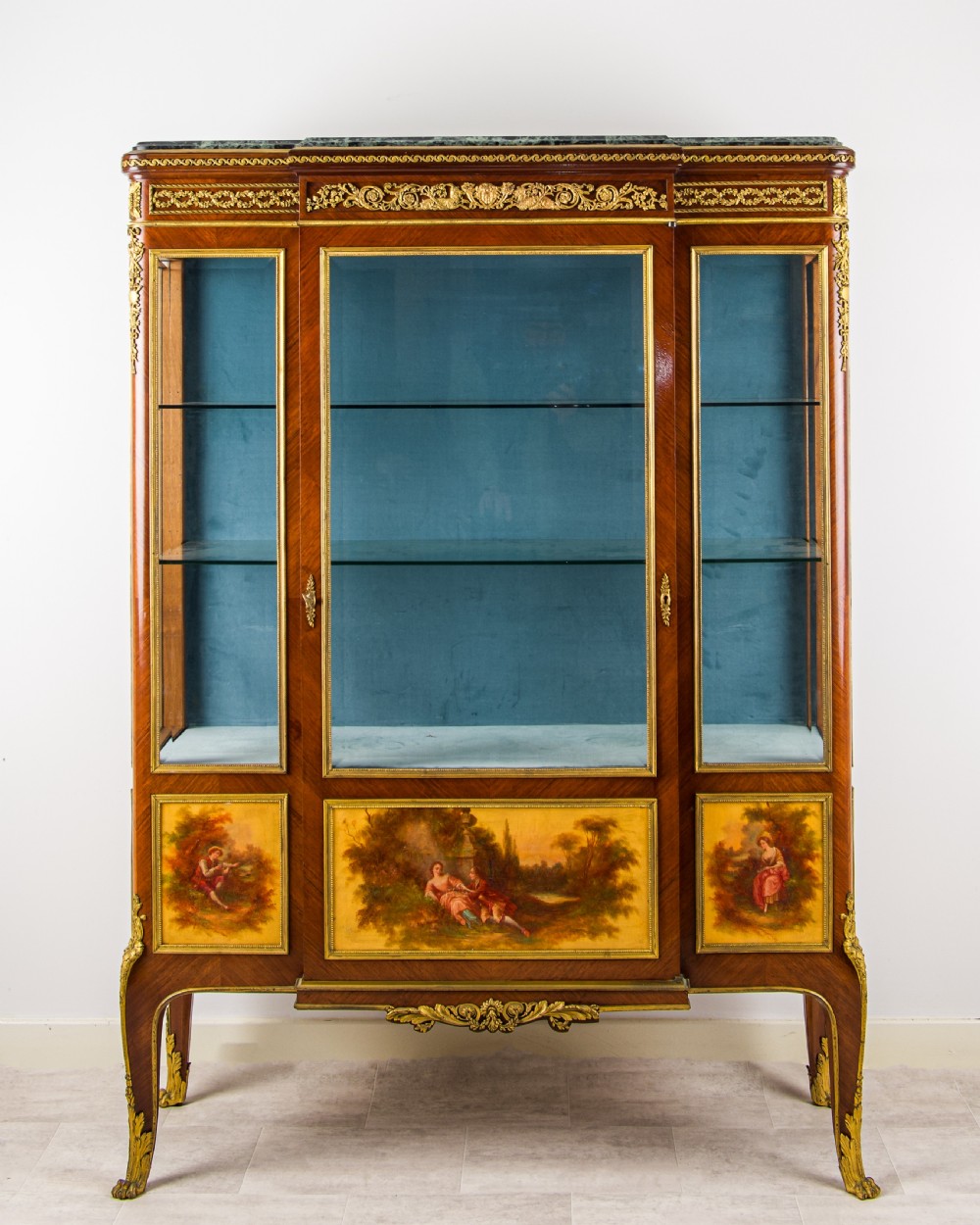 A French kingwood vitrine cabinet featuring glass display doors, gilt bronze mounts, a green marble top, blue fabric lining, and hand-painted Vernis Martin panels at the base.