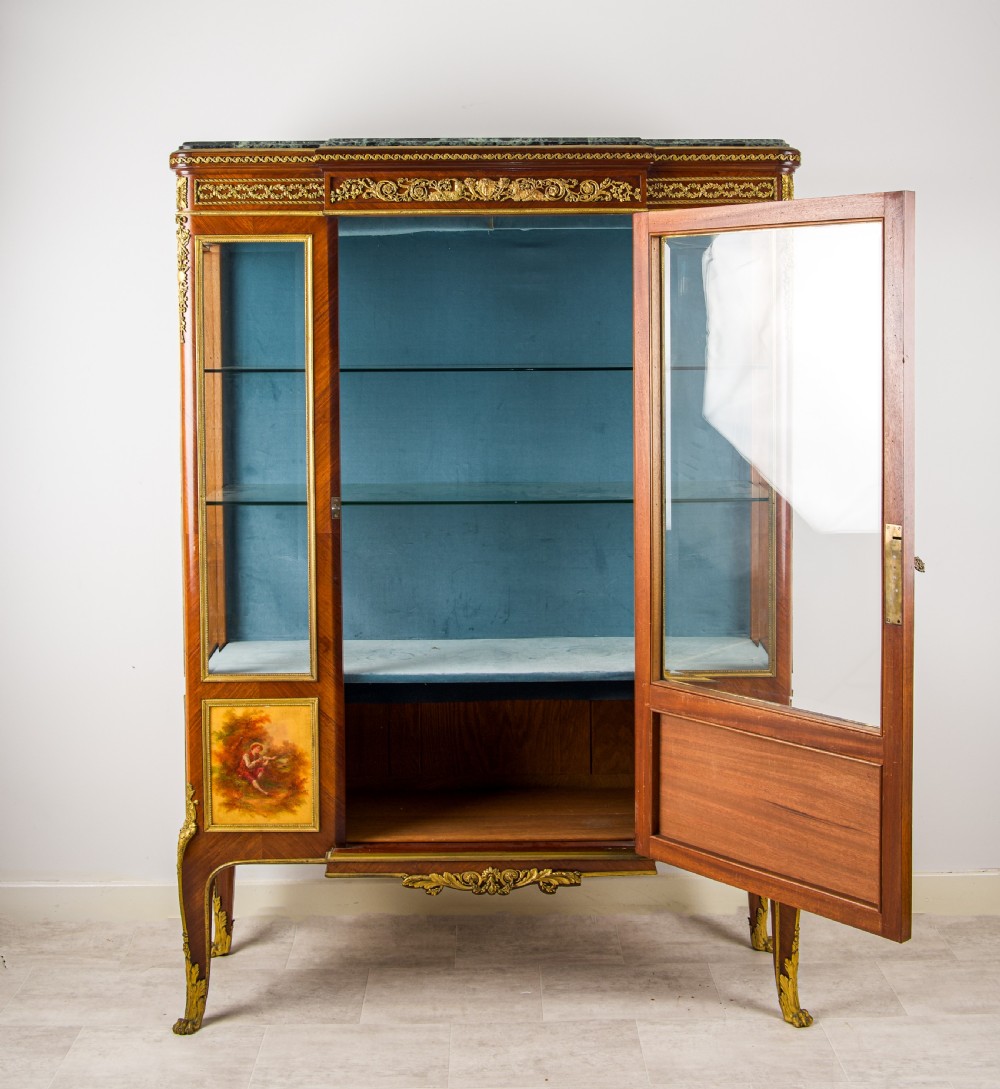 A French kingwood vitrine cabinet featuring glass display doors, gilt bronze mounts, a green marble top, blue fabric lining, and hand-painted Vernis Martin panels at the base. View VII