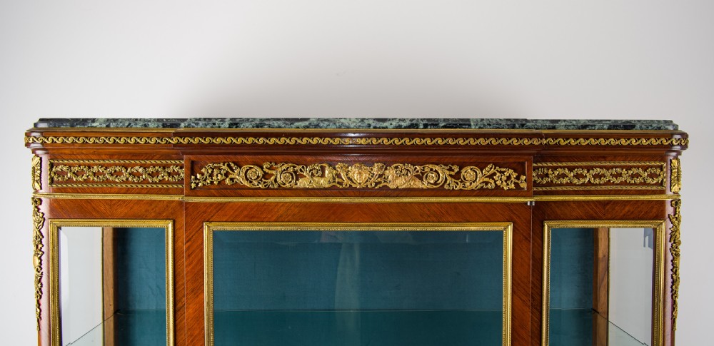 A French kingwood vitrine cabinet featuring glass display doors, gilt bronze mounts, a green marble top, blue fabric lining, and hand-painted Vernis Martin panels at the base. View IX