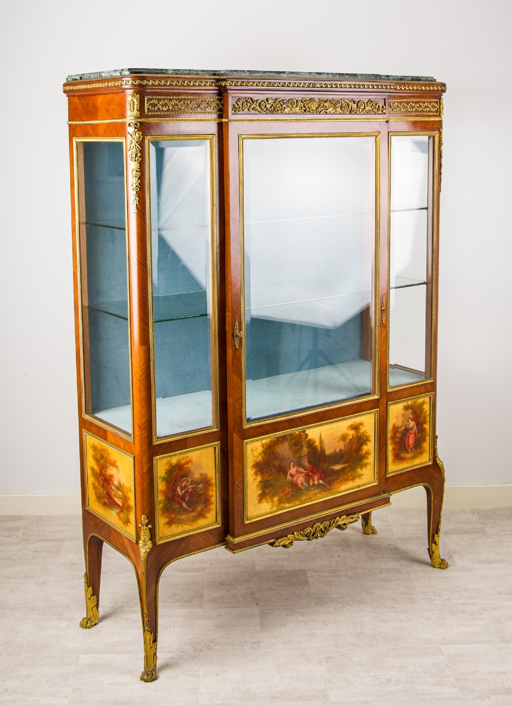 A French kingwood vitrine cabinet featuring glass display doors, gilt bronze mounts, a green marble top, blue fabric lining, and hand-painted Vernis Martin panels at the base. View X