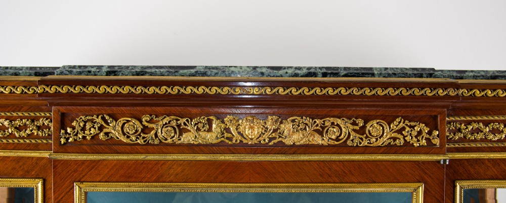 A French kingwood vitrine cabinet featuring glass display doors, gilt bronze mounts, a green marble top, blue fabric lining, and hand-painted Vernis Martin panels at the base. View XI
