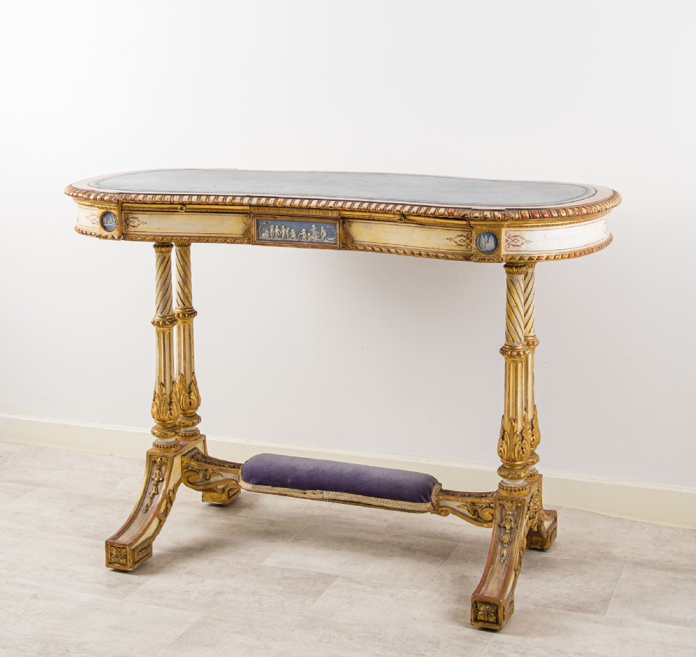 A 19th-century Neoclassical kidney-shaped writing table decorated in cream paint and gold leaf, featuring fluted legs, blue jasperware plaques, and a purple fabric-covered stretcher footrest. View III