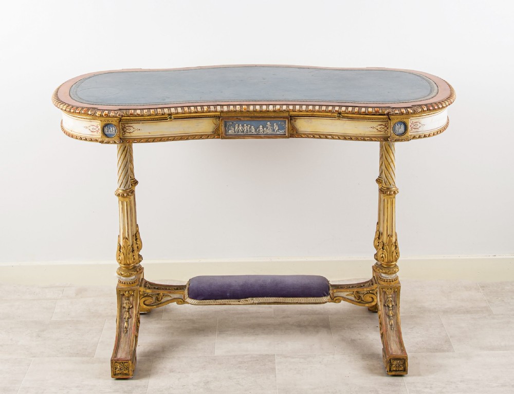A 19th-century Neoclassical kidney-shaped writing table decorated in cream paint and gold leaf, featuring fluted legs, blue jasperware plaques, and a purple fabric-covered stretcher footrest. View VIII