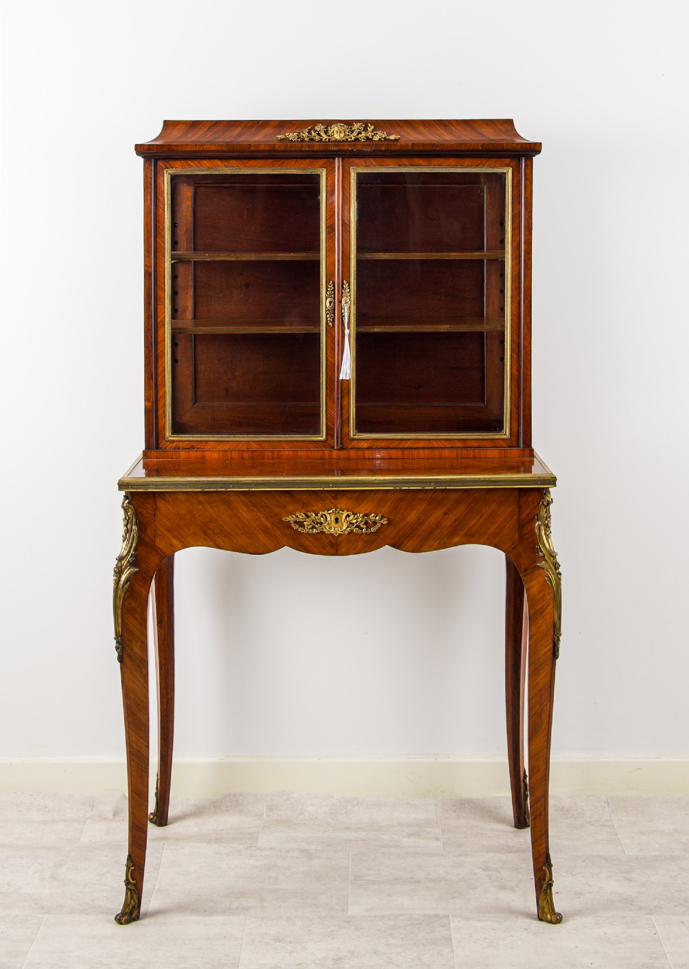 A 19th-century French kingwood bonheur du jour writing cabinet with glazed upper doors, ornate gilt-bronze mounts, and cabriole legs.