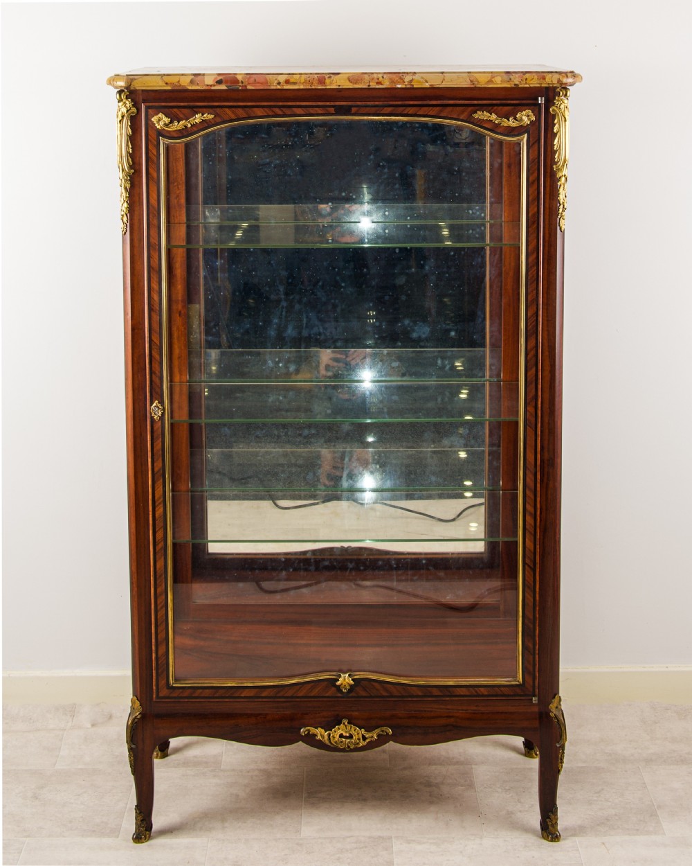 A French kingwood vitrine cabinet featuring gilt-bronze mounts, a marble top, a glazed single door, glass shelves, and cabriole legs. View IV