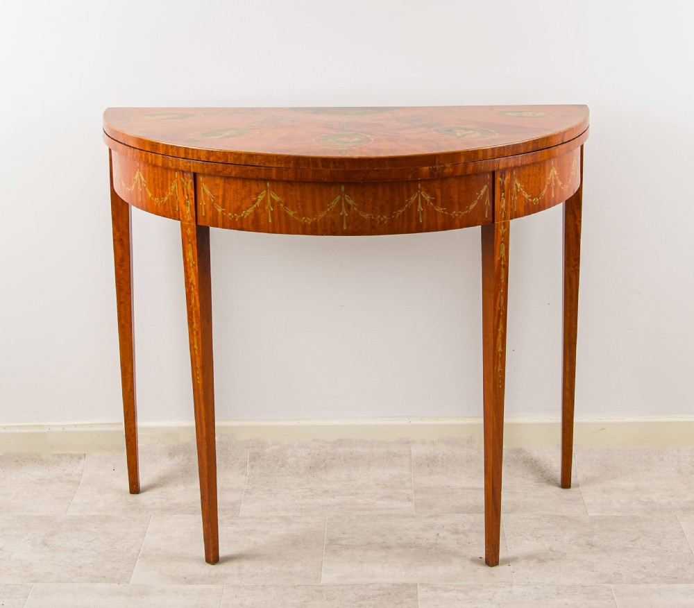 An antique satinwood demi-lune games table featuring hand-painted floral medallions and swags across the fold-over top and frieze. View IV