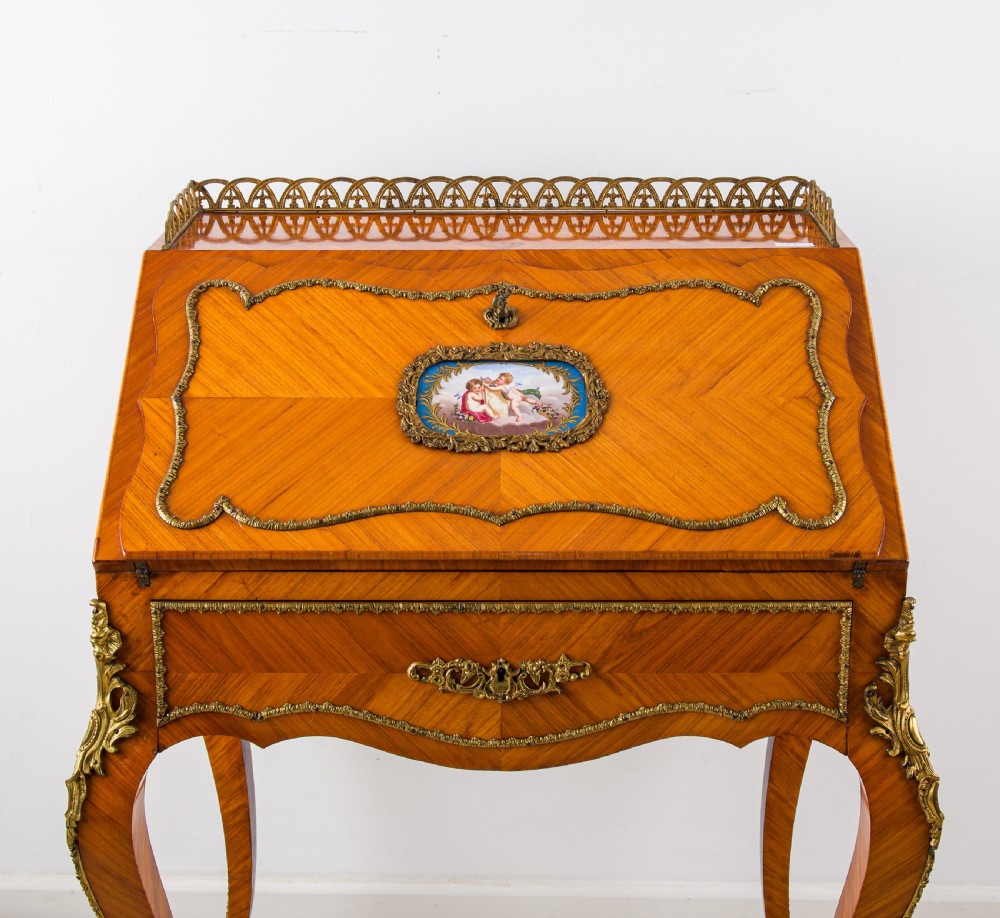 An antique French Louis XV style kingwood writing bureau with a slant-front lid featuring a central painted porcelain plaque, brass top gallery, cabriole legs, and gilded ormolu mounts. View IV