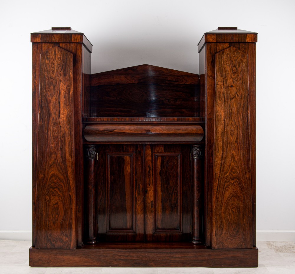 An antique William IV dark rosewood side cabinet featuring twin flanking pedestal towers, a central cupboard with panelled doors, turned column accents, and a low backboard.