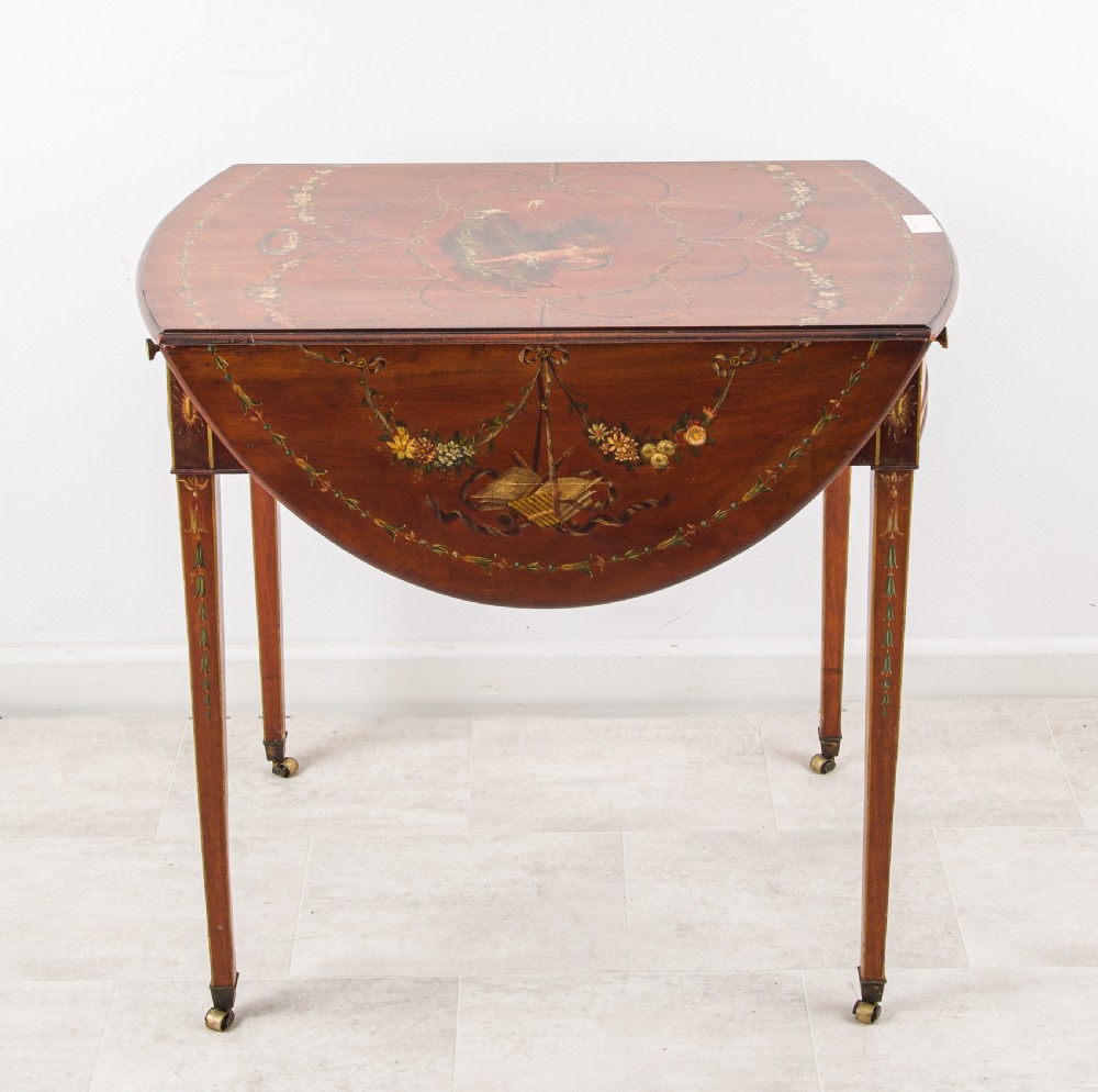 An antique mahogany Pembroke table featuring hand-painted floral swags, tapered legs with brass castors, and two hinged drop leaves. View II