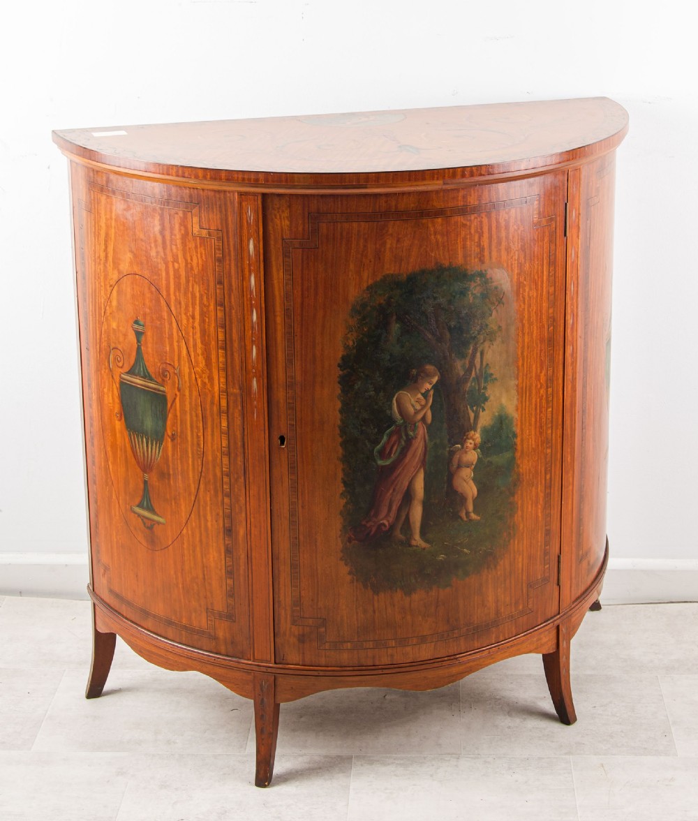 A late Victorian satinwood demi-lune side cabinet featuring hand-painted classical figures and urn panels on tapered legs.